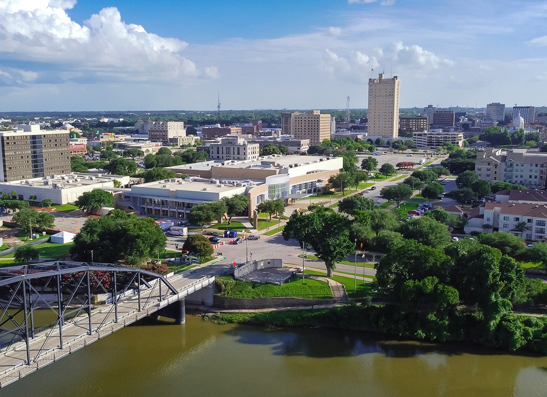 Waco, TX - Aerial View of Waco, TX With City Buildings and a Bridge Crossing a River on a Sunny Day